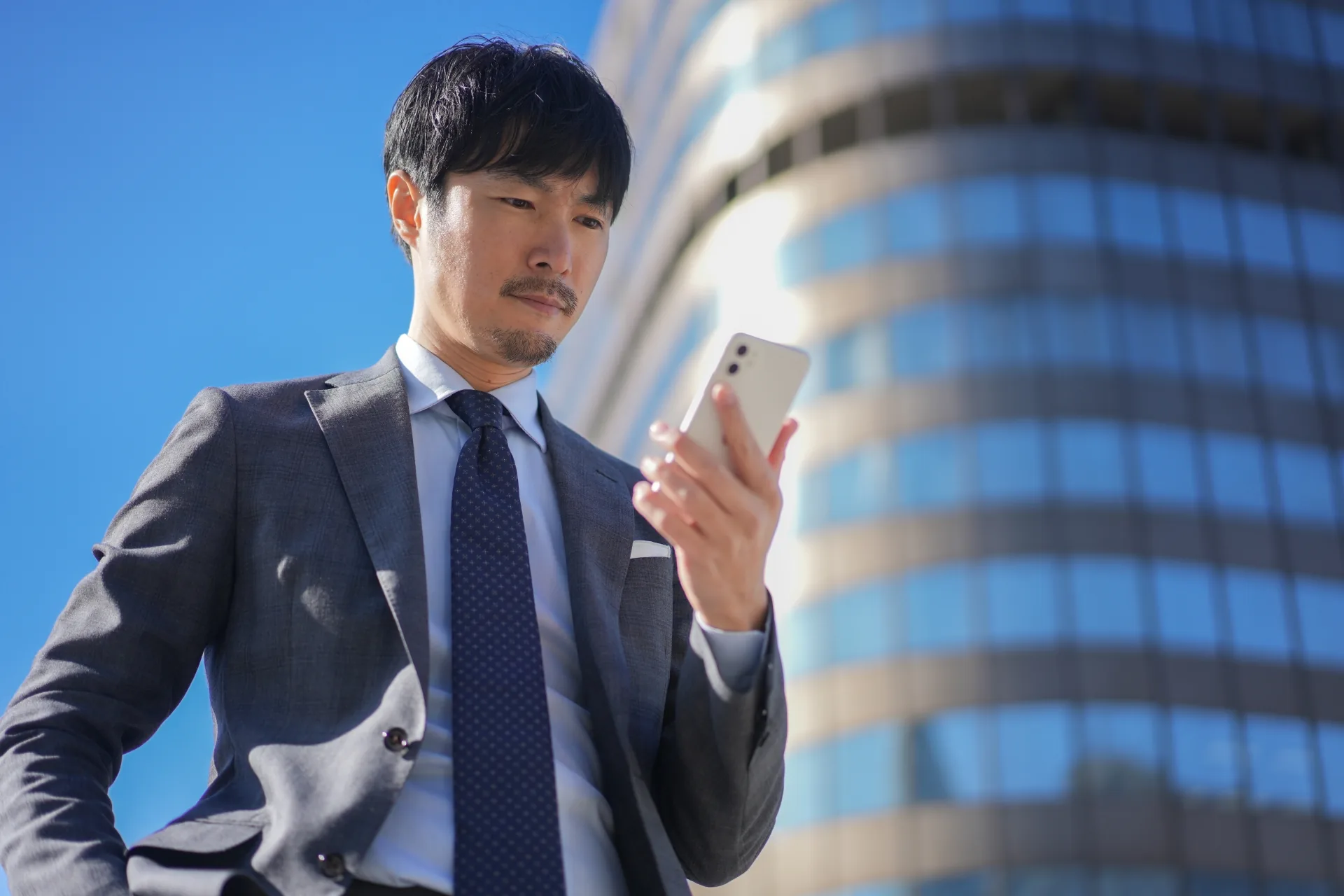 屋外でスマートフォンを確認するスーツ姿の男性