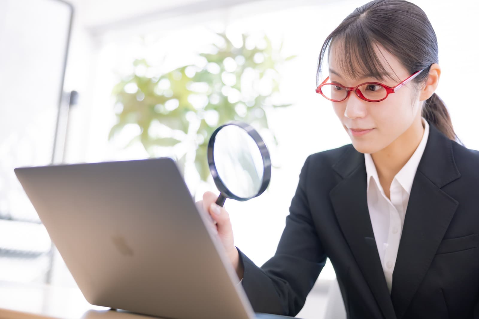 虫眼鏡とノートパソコンで転職サービスの情報を確認する女性社員