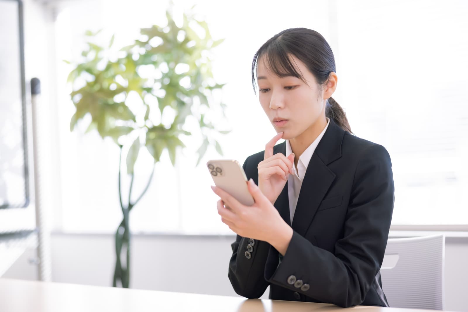 スマホを見ながら新卒で会社を辞めるか悩むスーツ姿の女性