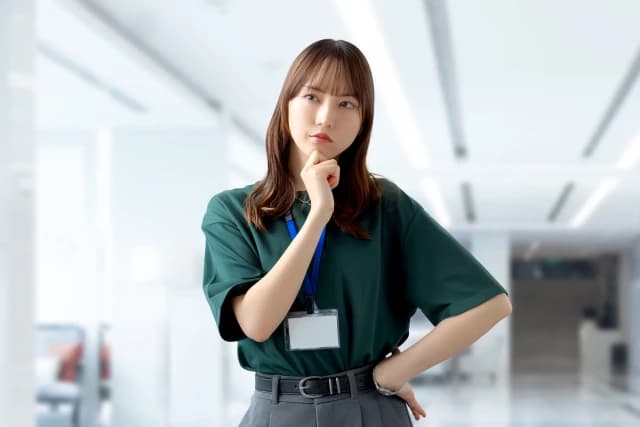 明るいオフィスで顎に手を添えて考える女性